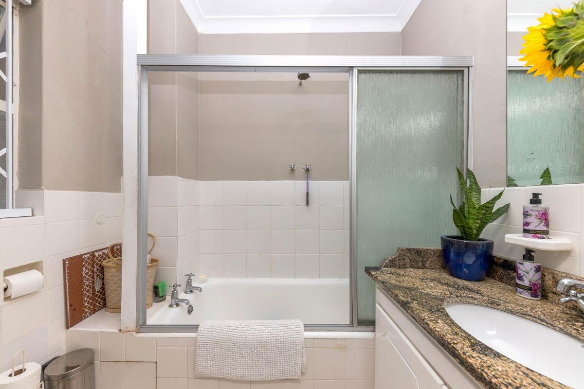 A functional bathroom featuring a shower-over-bath combination, granite-topped vanity, and neutral wall finishes, offering potential for cosmetic updates.