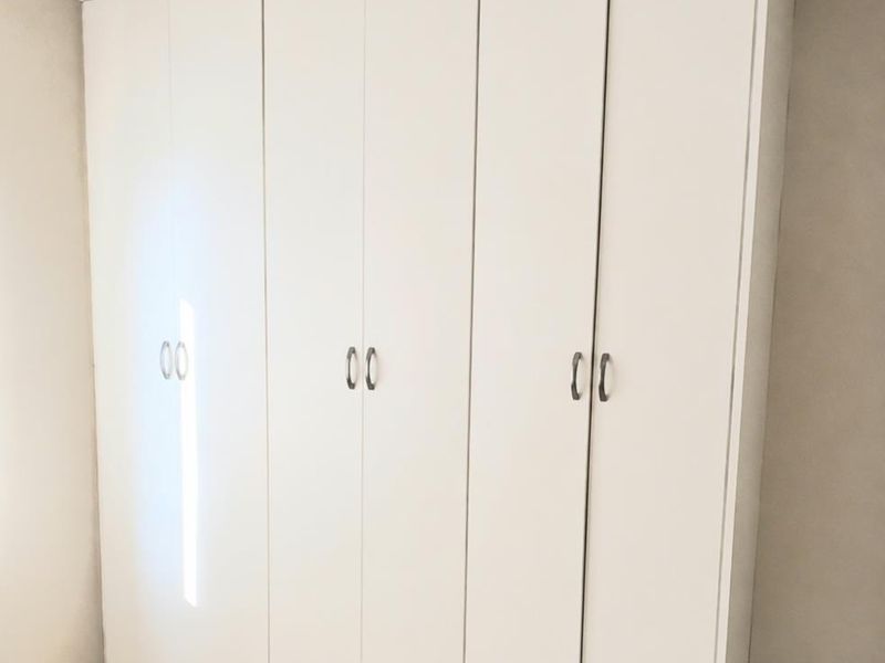 A clean bedroom interior featuring a large, white built-in wardrobe with modern handles and neutral tiled flooring.