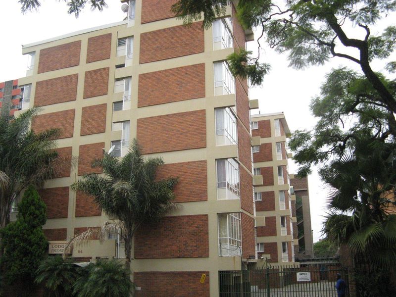 Exterior view of a multi-story apartment building featuring a brick facade and secure gated entrance.