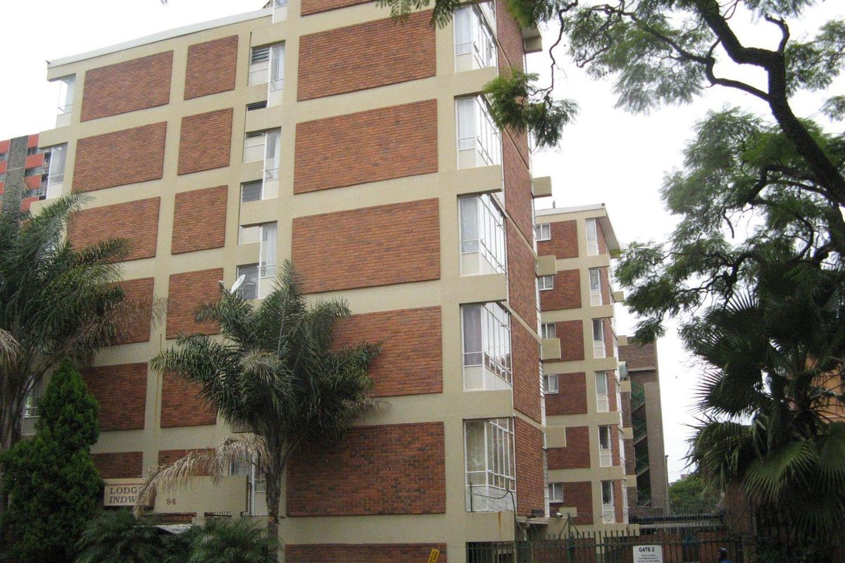 Exterior view of a multi-story apartment building featuring a brick facade and secure gated entrance.