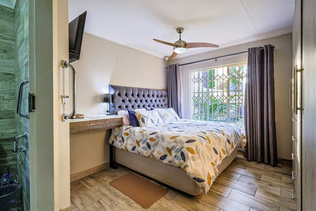 A well-maintained bedroom featuring tiled flooring, a ceiling fan, a built-in desk, and a security gate on the window.
