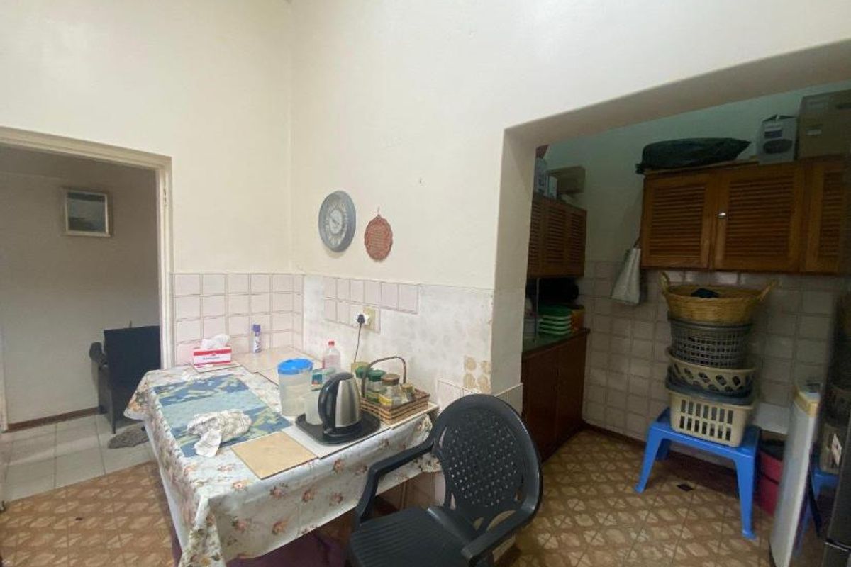 A dated kitchen and scullery area featuring tiled flooring, wall-mounted cabinetry, and tiled splashbacks, requiring modernization to improve functionality and aesthetic appeal.