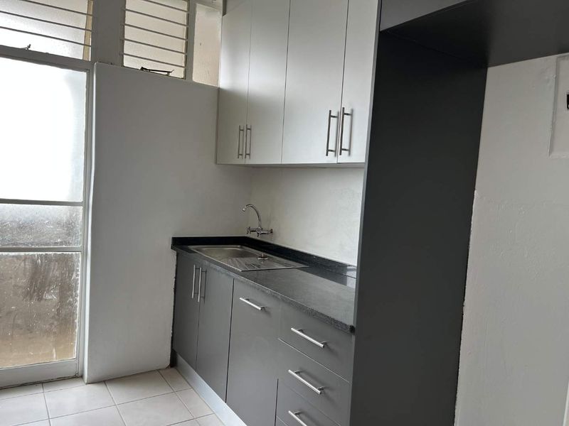 A clean, functional kitchen area featuring modern grey and white cabinetry, stone countertops, a stainless steel sink, and tiled flooring.