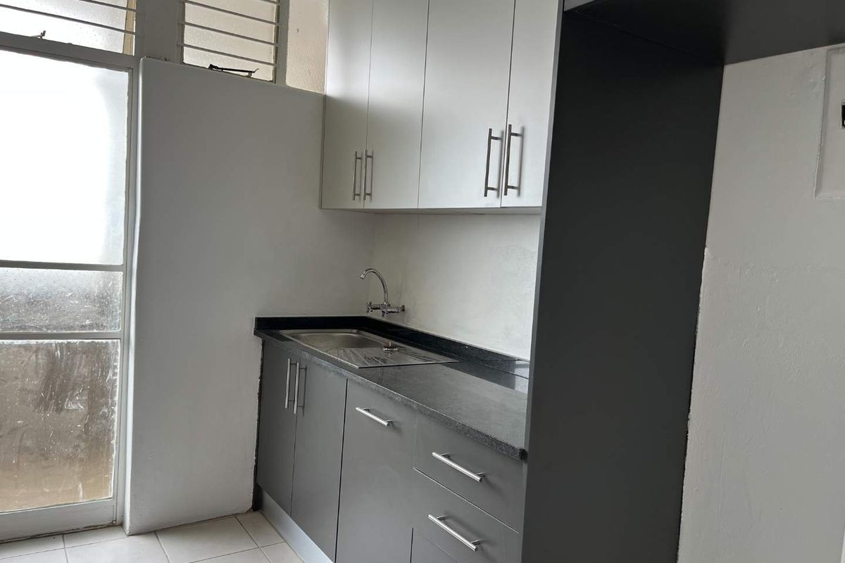 A clean, functional kitchen area featuring modern grey and white cabinetry, stone countertops, a stainless steel sink, and tiled flooring.