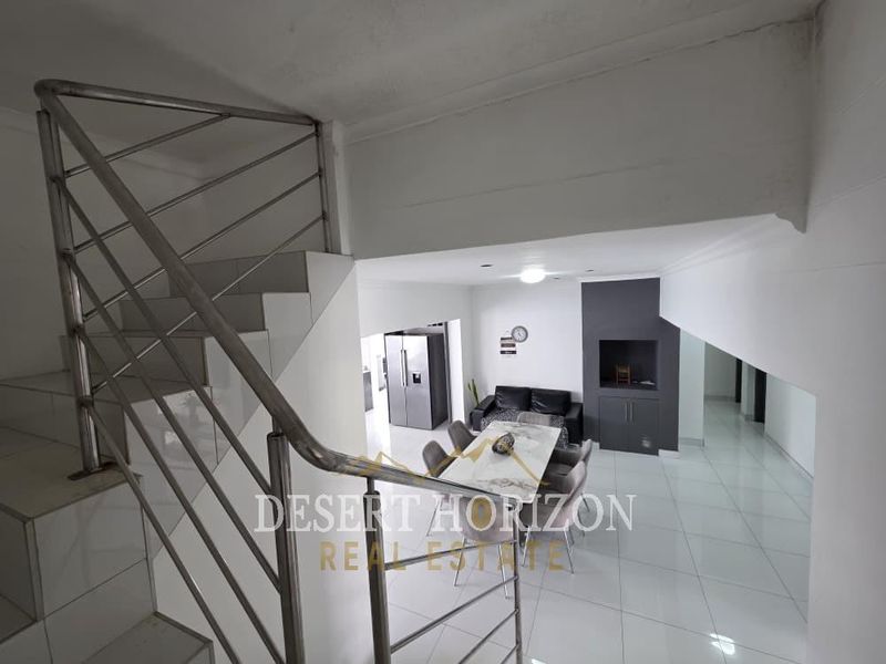 Open plan living and dining area featuring tiled floors, a built-in fireplace, and a modern stainless steel staircase railing.