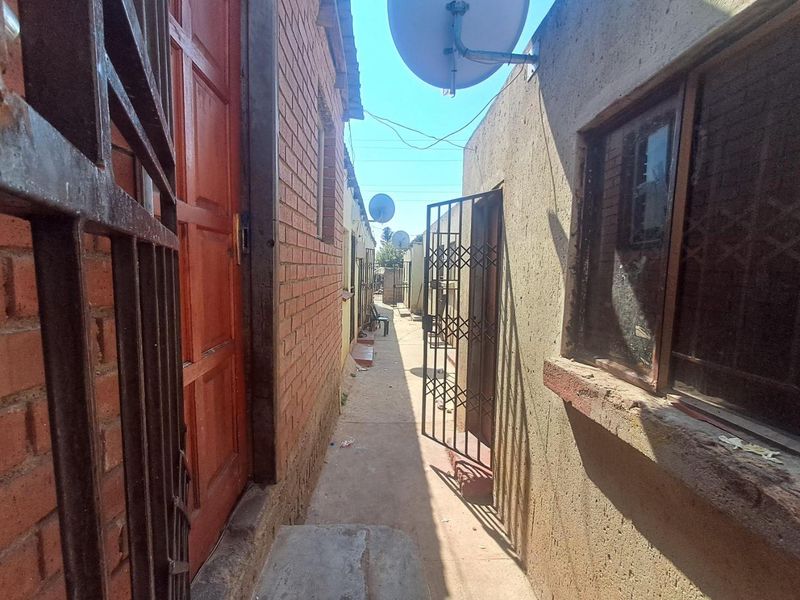 A narrow exterior side passage between two residential structures featuring brick and plastered walls, security gates, and concrete flooring.