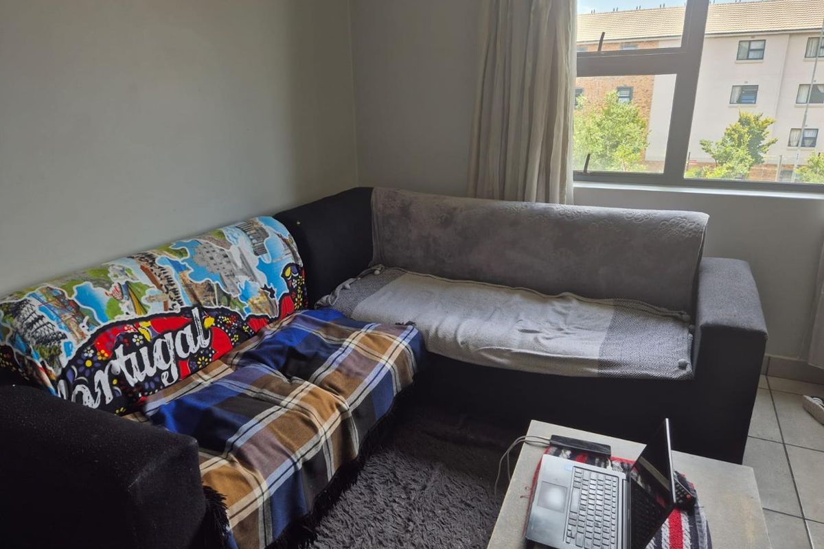 A living room area featuring tiled flooring and a large window providing natural light and views of the surrounding apartment complex.
