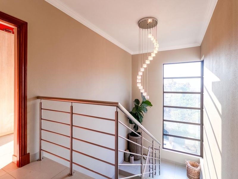 A bright staircase landing featuring a modern spiral chandelier, stainless steel balustrade, and large window providing natural light.