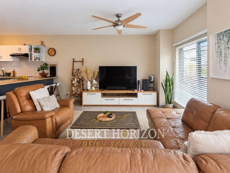 Open-plan living area featuring a modern kitchen with tiled backsplash and a comfortable lounge space with large windows and a ceiling fan.