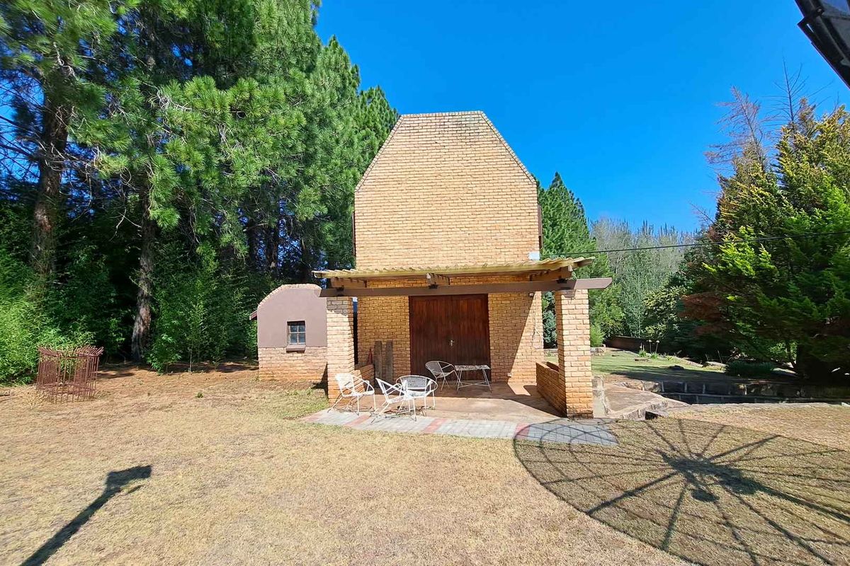A rustic brick outbuilding featuring a covered patio area, set within a spacious, tree-lined garden environment on the farm property.