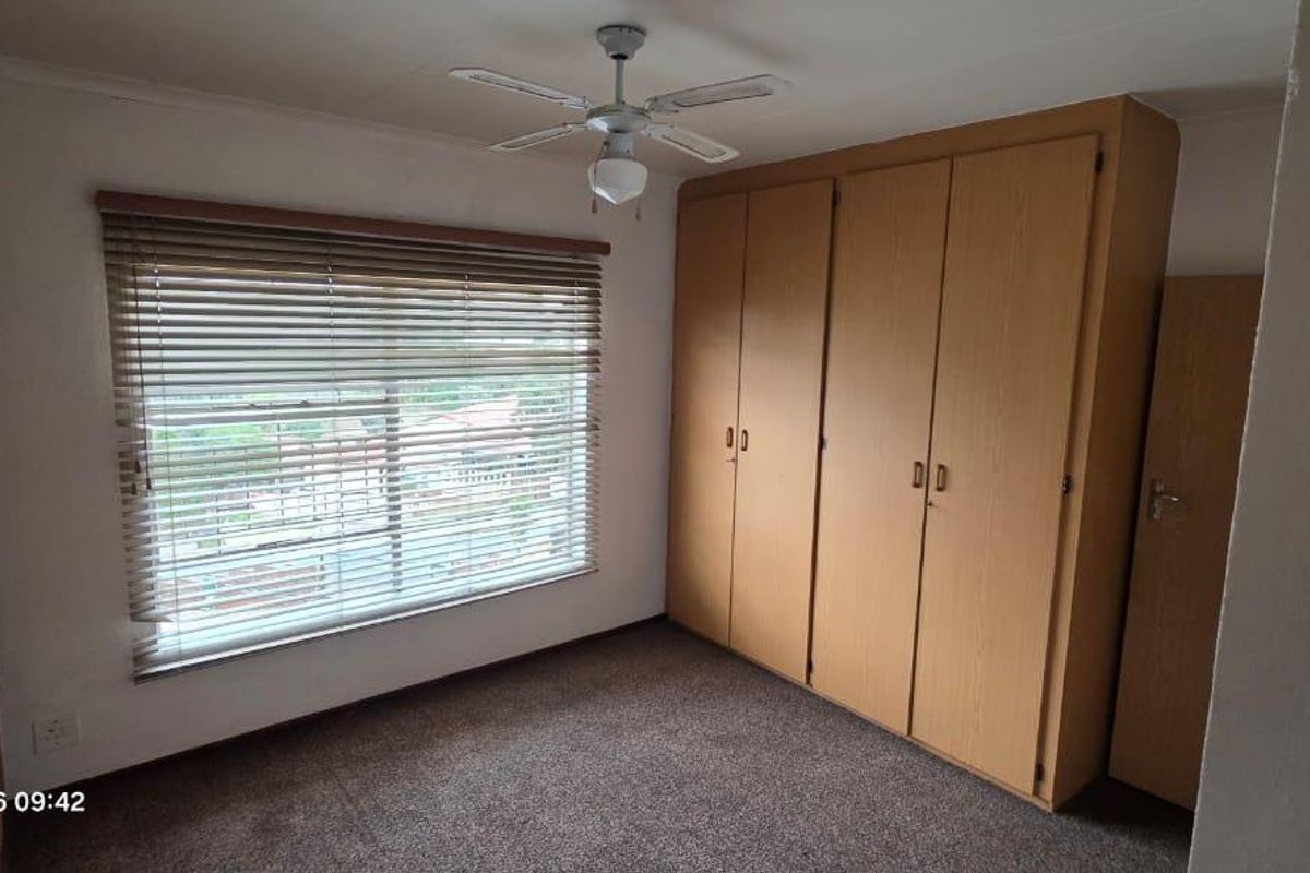 A bedroom featuring built-in wooden cupboards, a ceiling fan, venetian blinds, and a textured brick feature wall.