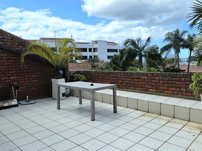 An open-air balcony featuring brick perimeter walls, tiled flooring, and a built-in raised tiled bench, offering an elevated outdoor space.