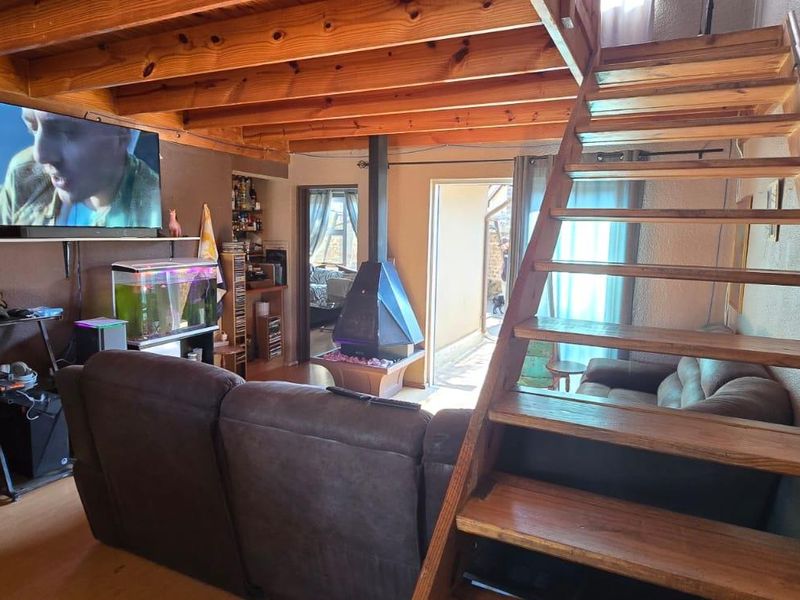 Living room featuring exposed timber ceiling beams, a central freestanding fireplace, and a timber staircase leading to an upper level.