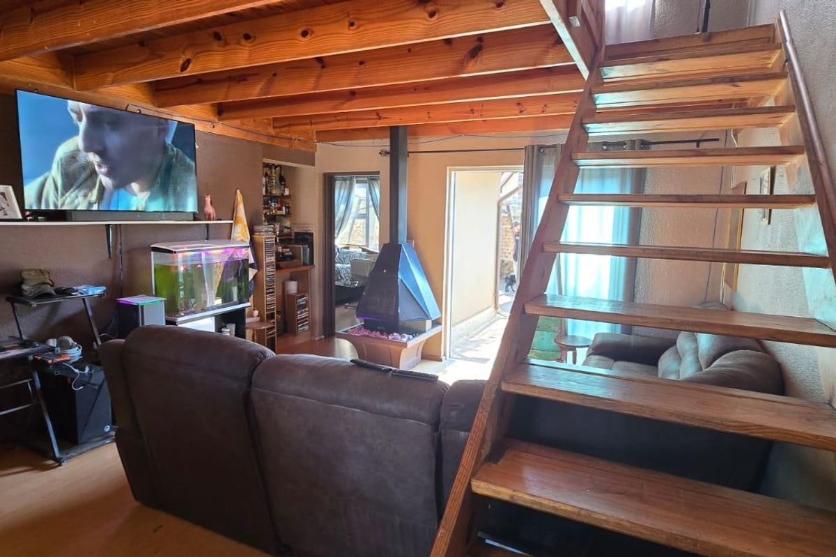 Living room featuring exposed timber ceiling beams, a central freestanding fireplace, and a timber staircase leading to an upper level.