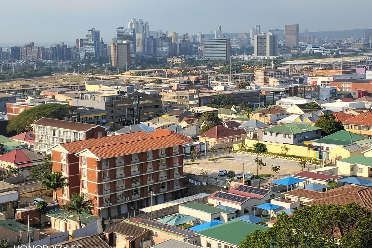 Elevated aerial view overlooking a dense urban neighborhood with a mix of residential apartment buildings and commercial infrastructure under a clear sky.