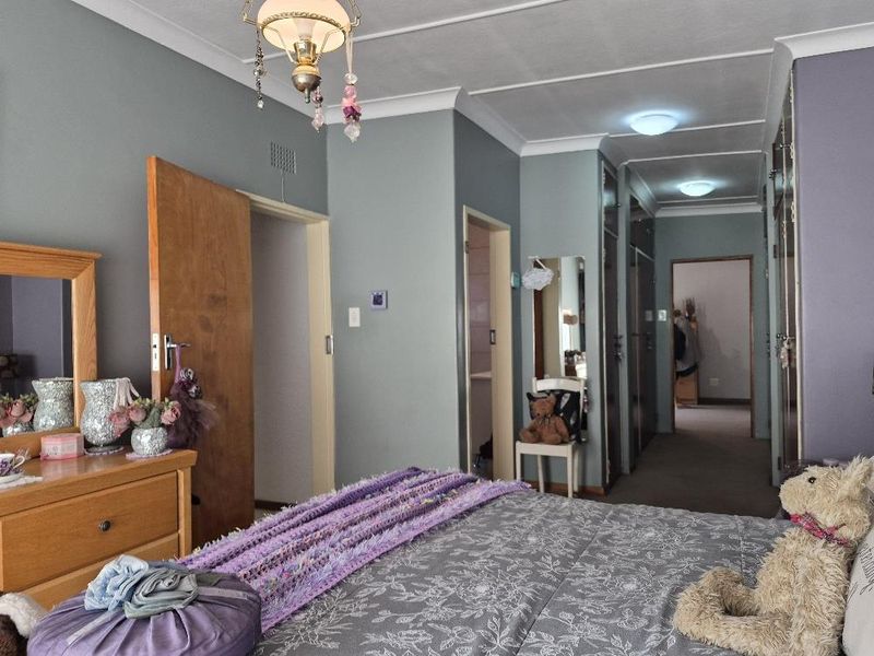 A bedroom featuring built-in cupboards, cove cornicing, and neutral wall finishes, providing a functional layout with direct access to an adjoining space.