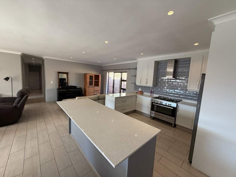 Spacious open-plan kitchen featuring a large island, quartz countertops, subway tile backsplash, and modern stainless steel appliances, seamlessly flowing into the living area.