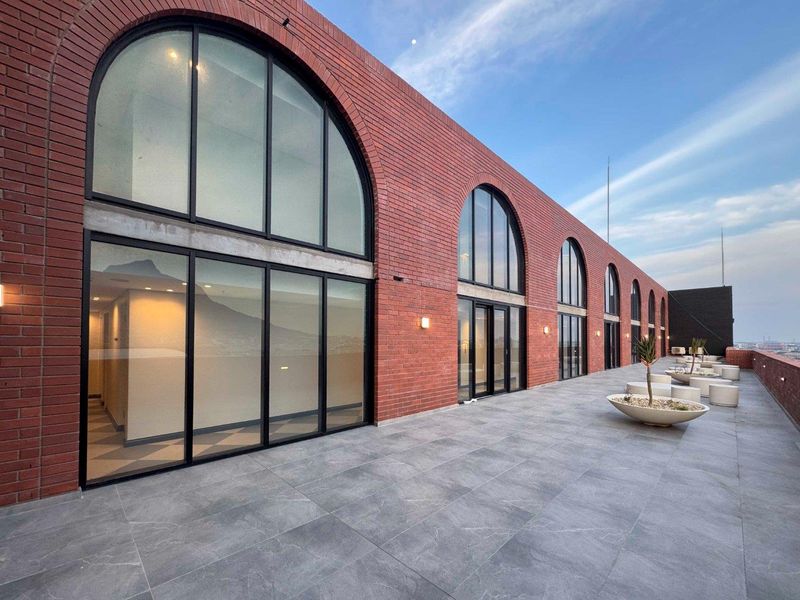 Spacious outdoor balcony featuring modern grey tiling, striking exposed brickwork, and large arched windows providing ample natural light to the interior.