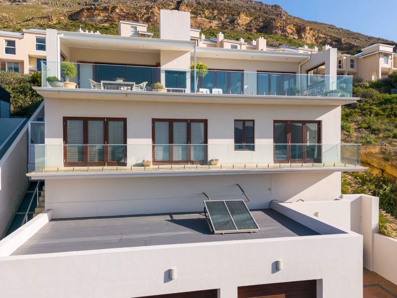 Rear elevation of a multi-level residence featuring glass balustrades, expansive sliding doors, and a solar water heating system on the flat roof section.