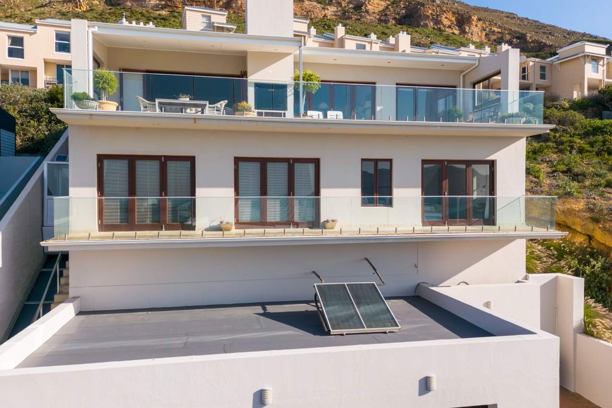 Rear elevation of a multi-level residence featuring glass balustrades, expansive sliding doors, and a solar water heating system on the flat roof section.