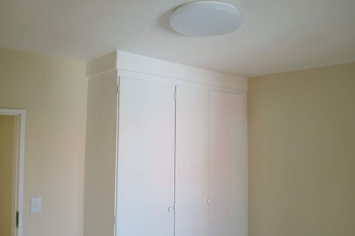 A clean, empty bedroom featuring a white built-in wardrobe and a simple flush mount ceiling light fixture.