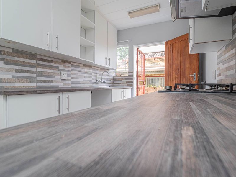 A clean, modern kitchen featuring white cabinetry, wood-look laminate countertops, a gas hob, and a tiled backsplash, with direct access to the exterior.