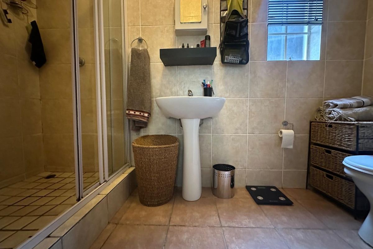 A functional bathroom featuring a pedestal basin, a glass-enclosed shower, and tiled walls and flooring.
