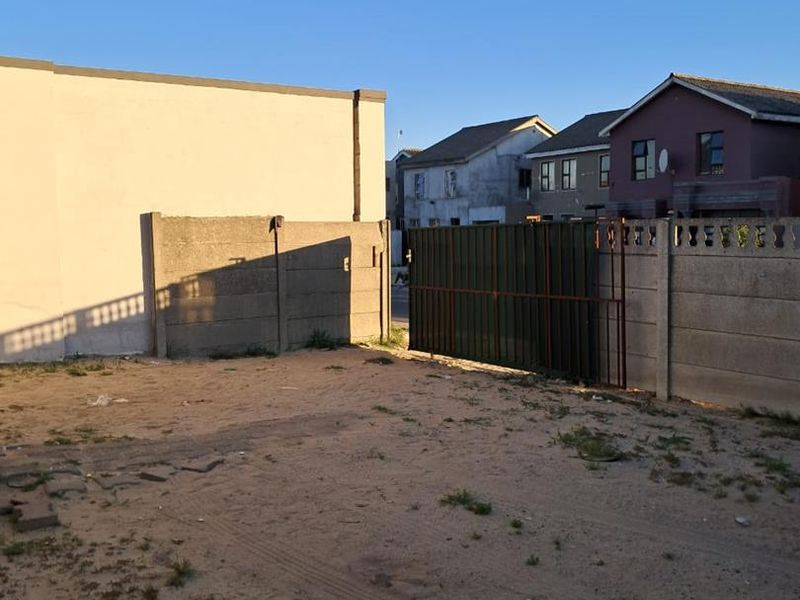 An unpaved rear yard area enclosed by precast concrete boundary walls and a metal gate, showing signs of neglect and lack of landscaping.