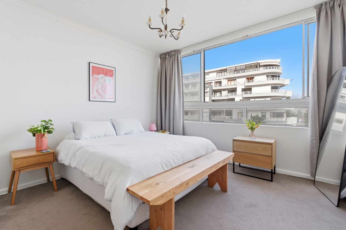 A bright and well-maintained bedroom featuring large sliding windows that provide ample natural light and an urban outlook.