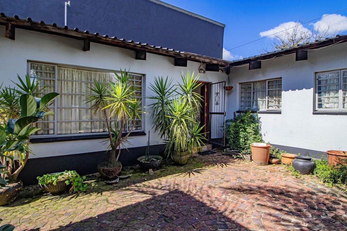 A private rear courtyard featuring brick paving, established garden elements, and direct access to the home through a security gate.