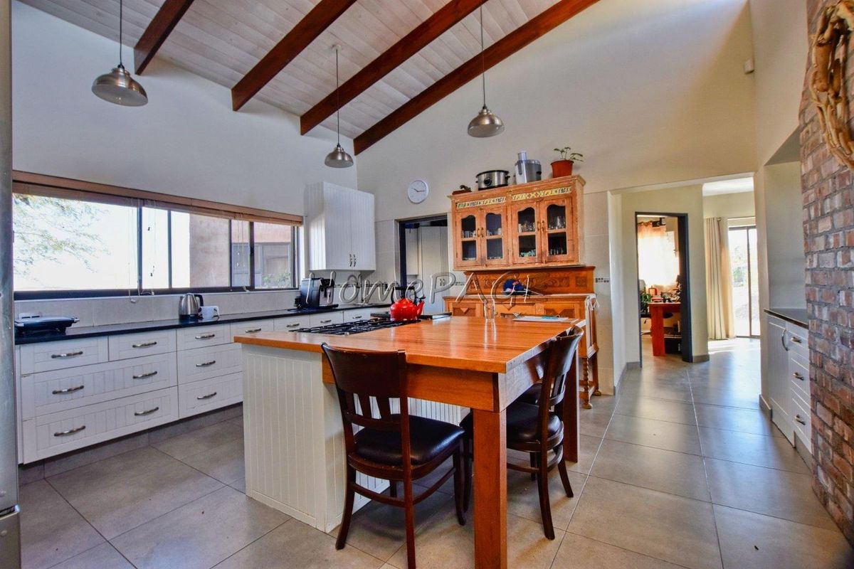 Spacious kitchen featuring a central wooden island with a built-in gas hob, white cabinetry, tiled flooring, and exposed timber ceiling beams.