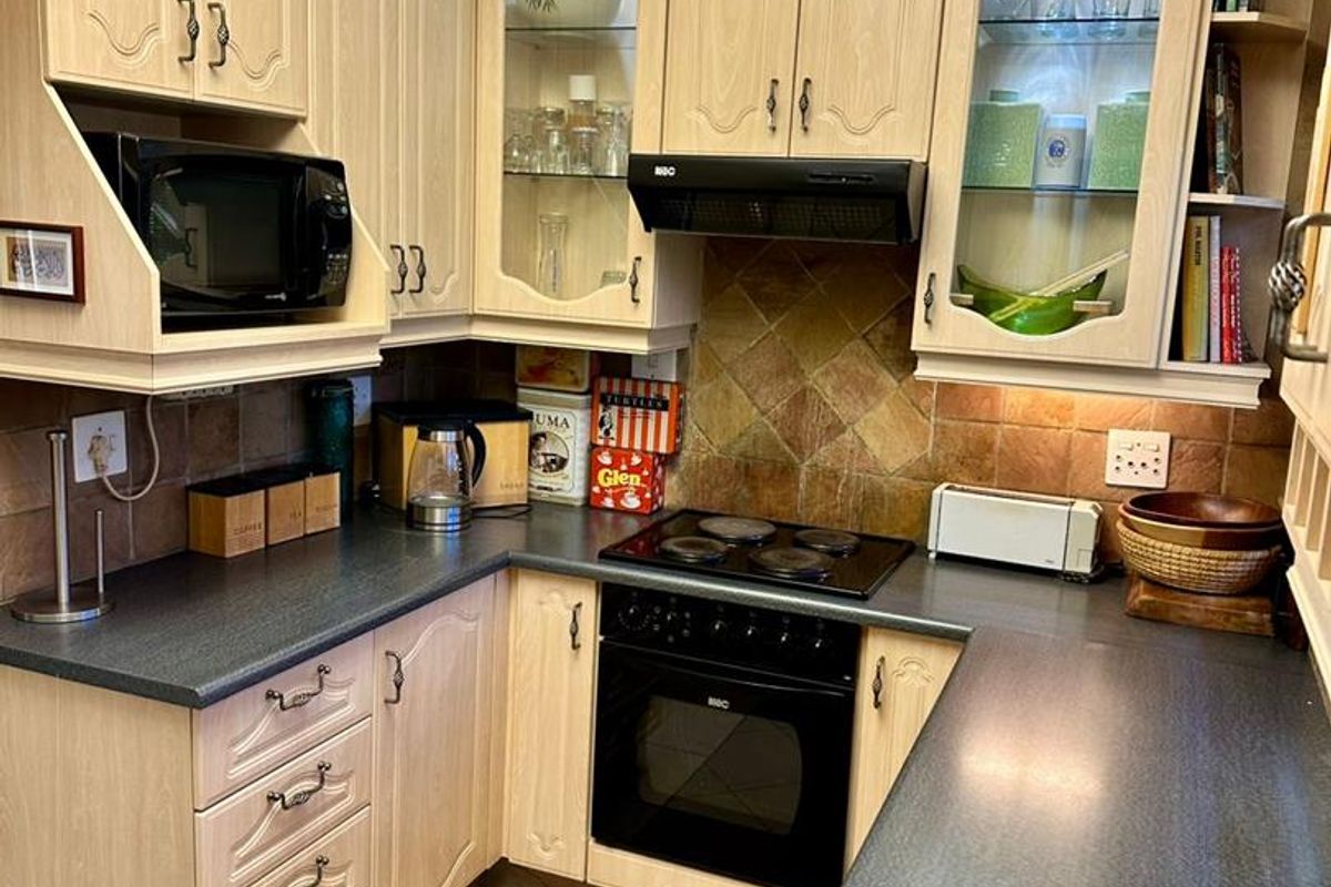 A functional kitchen featuring light wood-toned cabinetry, dark laminate countertops, a built-in oven, electric hob, and a tiled backsplash.