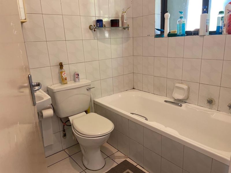 A compact bathroom featuring a standard bathtub, toilet, and tiled walls. The space is dated and would benefit from modern updates.