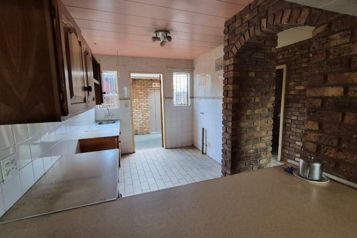 A dated kitchen featuring exposed brickwork, tiled flooring, and built-in cabinetry, offering a functional layout with potential for modern renovation.