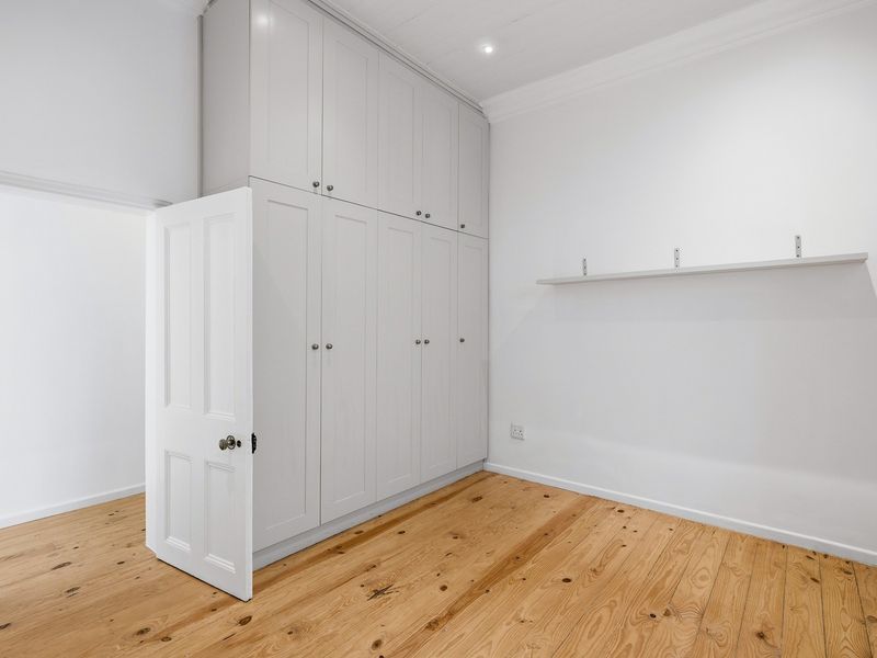 A bright, empty bedroom featuring polished timber flooring, extensive floor-to-ceiling built-in cabinetry, and a wall-mounted shelf.