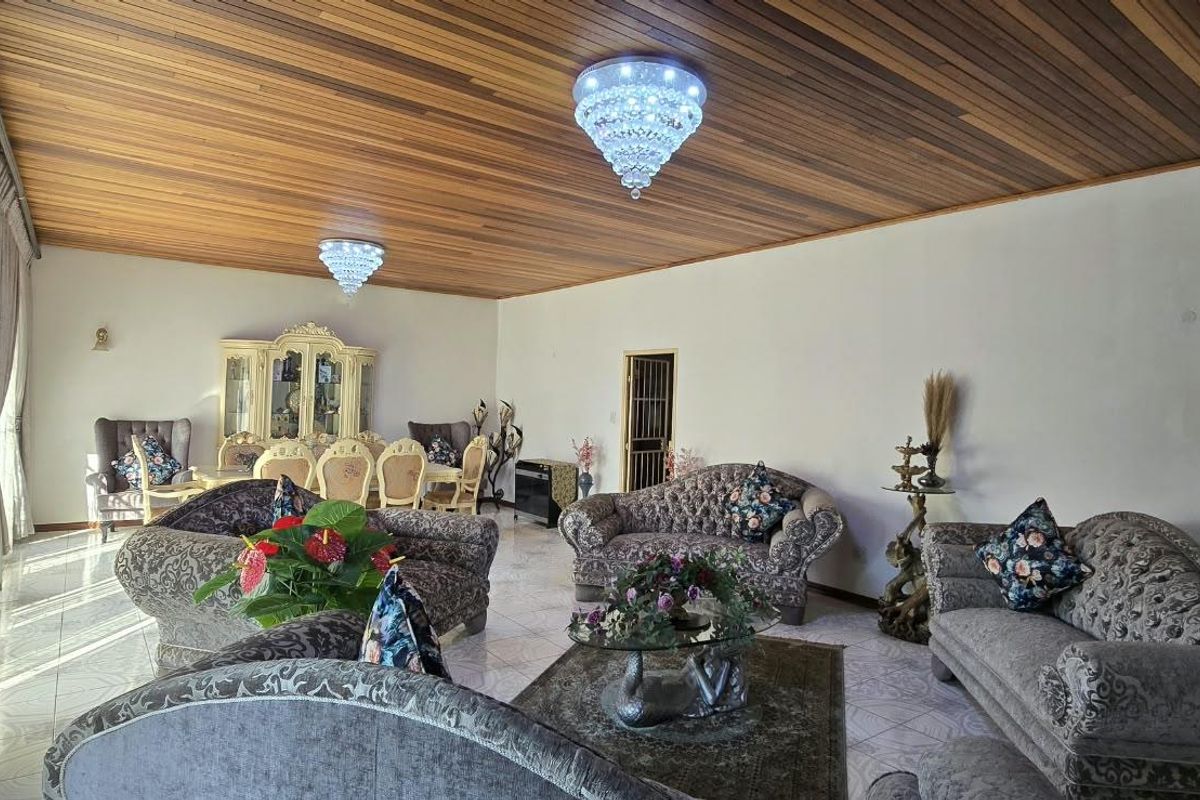 Spacious living room featuring a distinctive timber-clad ceiling, elegant crystal chandeliers, and neutral tiled flooring throughout.