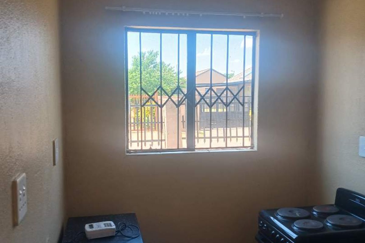 A compact kitchen area featuring tiled flooring, a built-in countertop, and a freestanding stove, with security bars installed on the window.