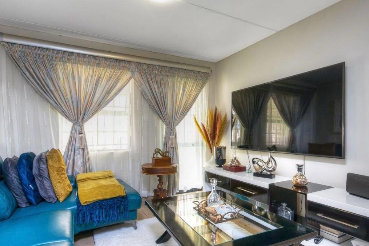 A comfortable living room featuring a wall-mounted television and large windows with curtains, providing a functional and inviting space for relaxation.