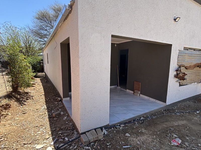 Rear view of the property showing a covered patio area with tiled flooring and unfinished exterior grounds requiring landscaping and repairs to the wall cladding.
