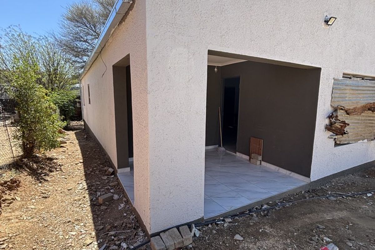 Rear view of the property showing a covered patio area with tiled flooring and unfinished exterior grounds requiring landscaping and repairs to the wall cladding.