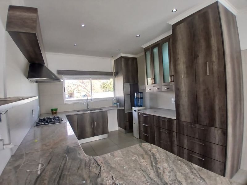 Modern kitchen featuring dark wood cabinetry, granite countertops, a gas hob, and a stainless steel extractor fan with recessed lighting.