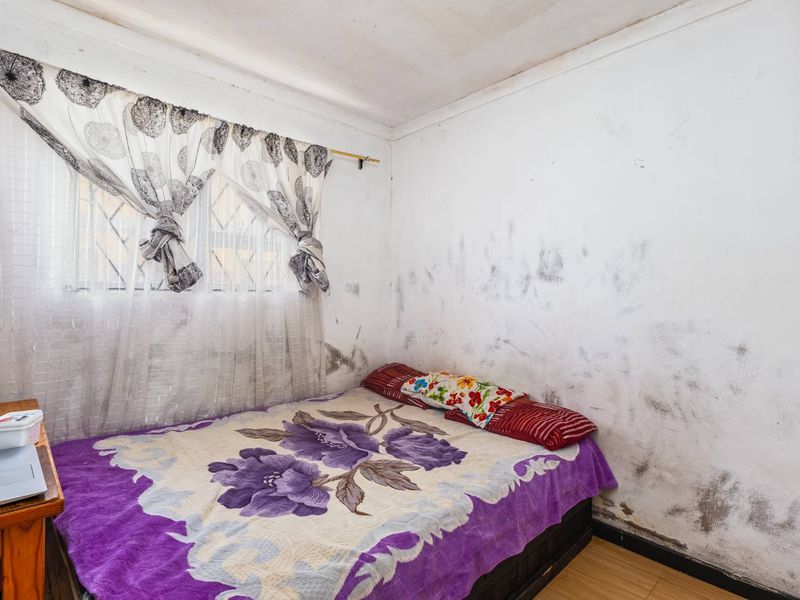A bedroom featuring laminate flooring and security bars on the window, currently showing significant wall surface deterioration requiring maintenance and repair.