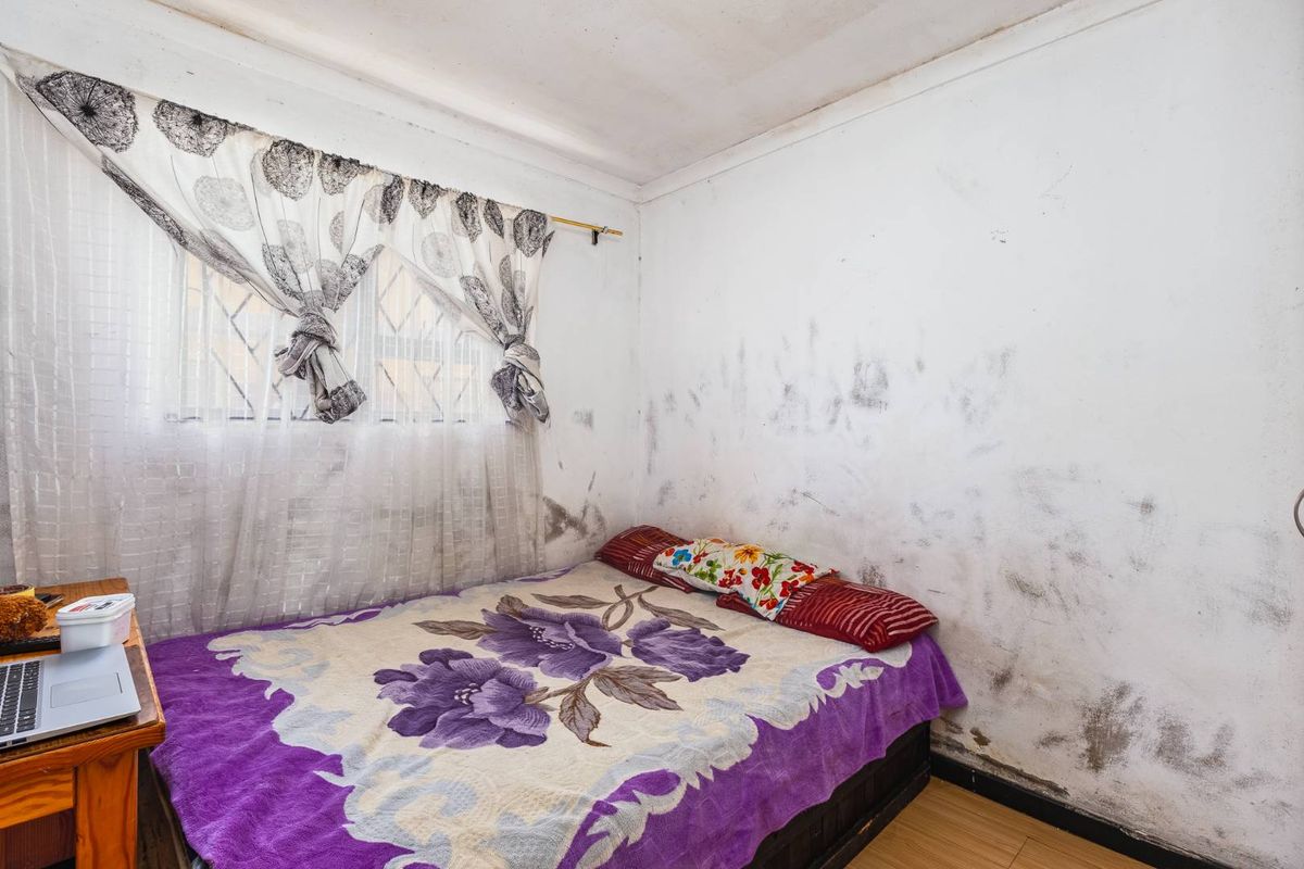 A bedroom featuring laminate flooring and security bars on the window, currently showing significant wall surface deterioration requiring maintenance and repair.