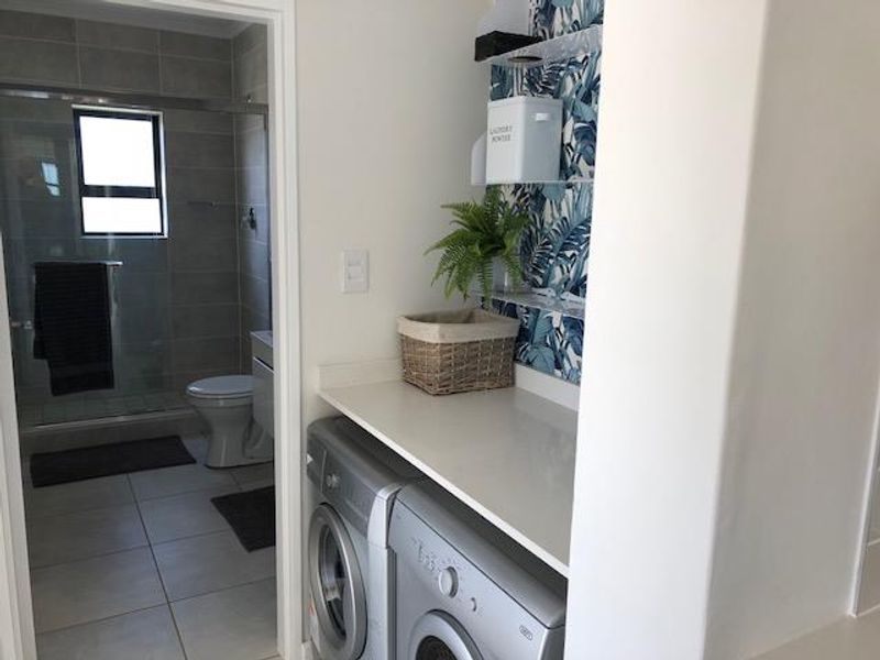 A functional laundry area featuring a built-in countertop, adjacent to a modern bathroom with a glass-enclosed shower and tiled finishes.