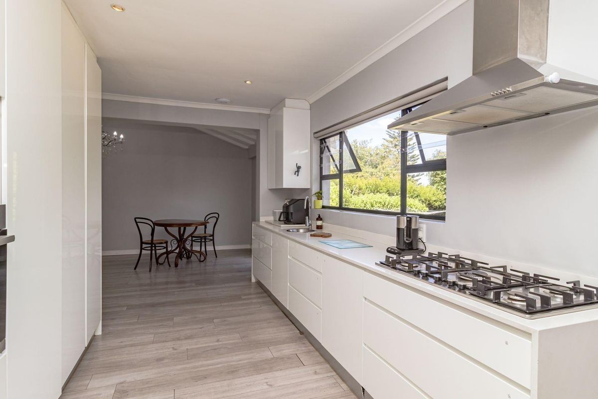 Modern galley-style kitchen featuring sleek white cabinetry, integrated oven, gas hob with extractor fan, and light wood-look flooring.