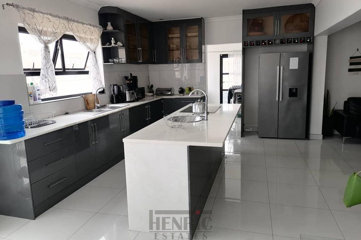 Modern kitchen featuring dark grey cabinetry, white stone countertops, a central island with a prep sink, and polished floor tiles.