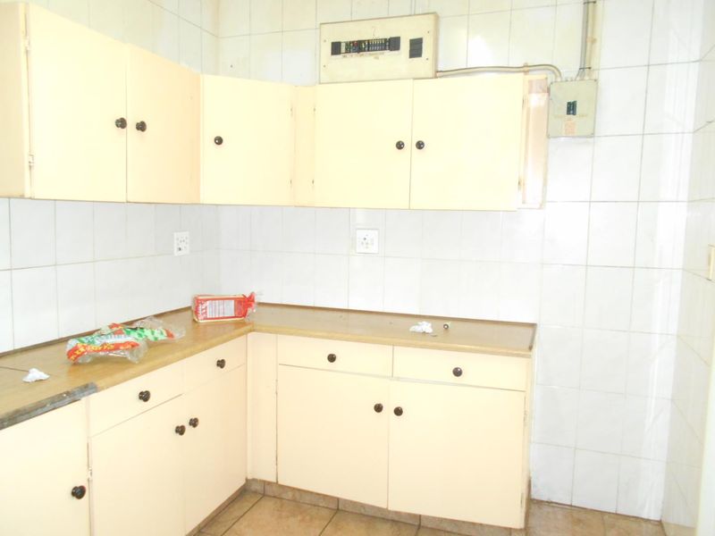 A dated kitchen area featuring built-in cabinetry, laminate countertops, and full-height wall tiling, currently vacant and ready for renovation.