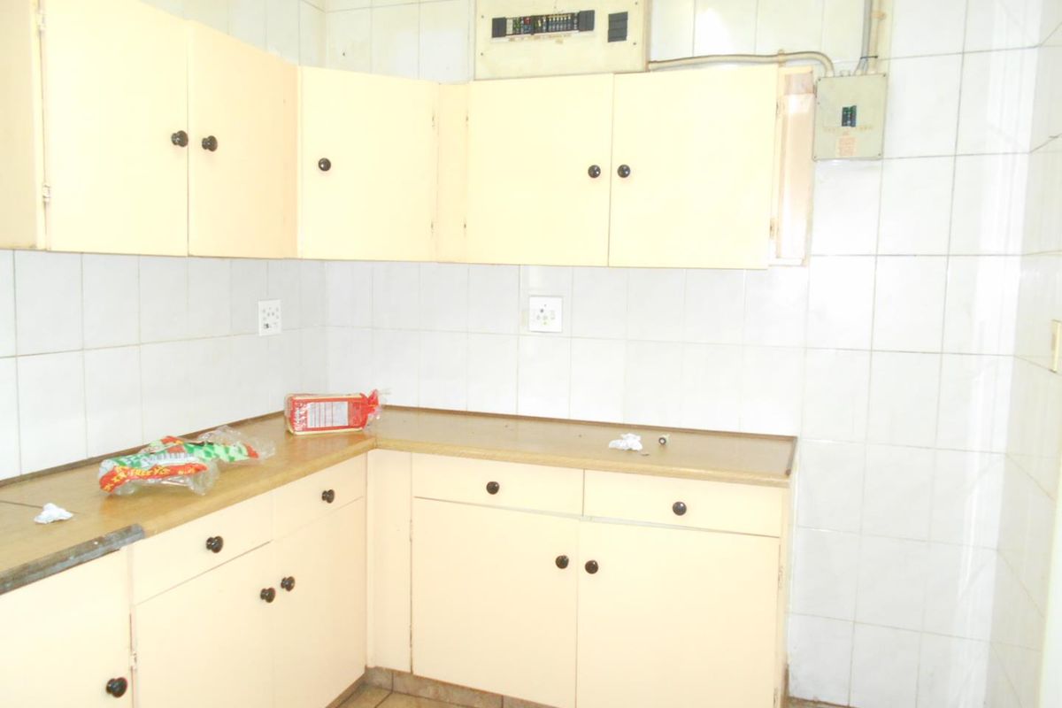 A dated kitchen area featuring built-in cabinetry, laminate countertops, and full-height wall tiling, currently vacant and ready for renovation.