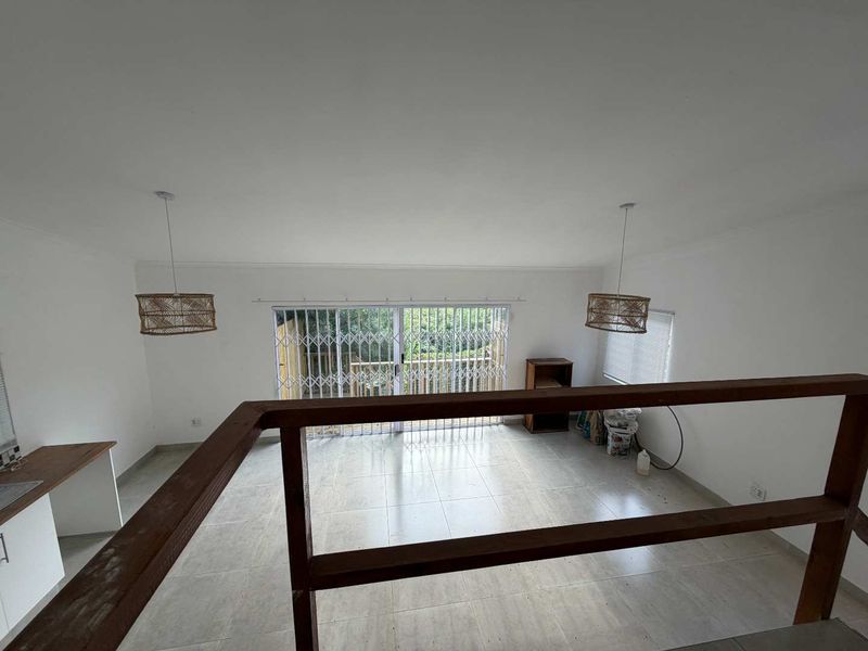 An open-plan living area featuring tiled flooring, a wooden balustrade, and a sliding glass door with security gate leading to an outdoor space.