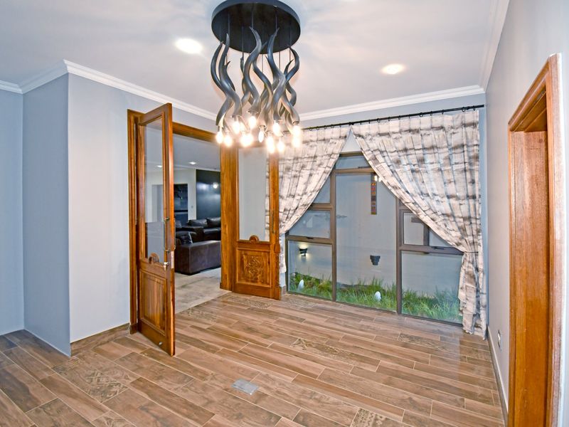 A bright, empty living space featuring wood-look tile flooring, crown molding, and a unique decorative chandelier, with access to an adjacent room.